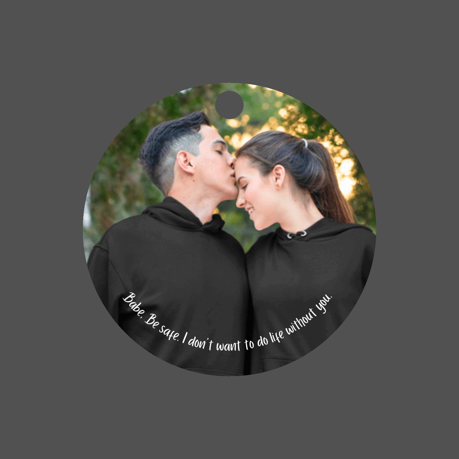 Car mirror hanging accessory ornament featuring a personalized photo of a couple in black hoodies shares a tender moment outdoors as the man kisses the woman's forehead. Text below reads, "Babe, be safe, I don't want to do life without you." These make great gifts for women and men.