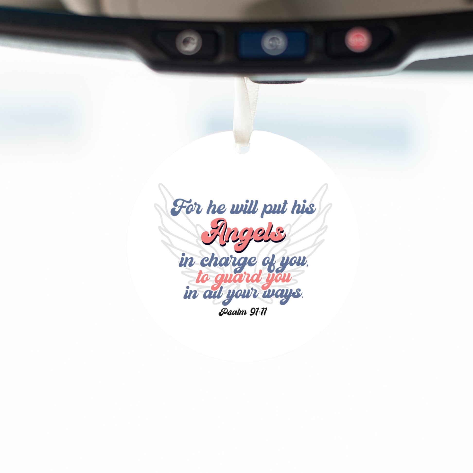 Close-up view inside vehicle of a round white car mirror hanging accessory ornament with white ribbon and the Bible verse Psalm 91:11, featuring angel wings. The text, in blue and red, conveys protection and guardianship. Makes a great gift for women, men, teenagers, and anyone who drives a lot in their work.