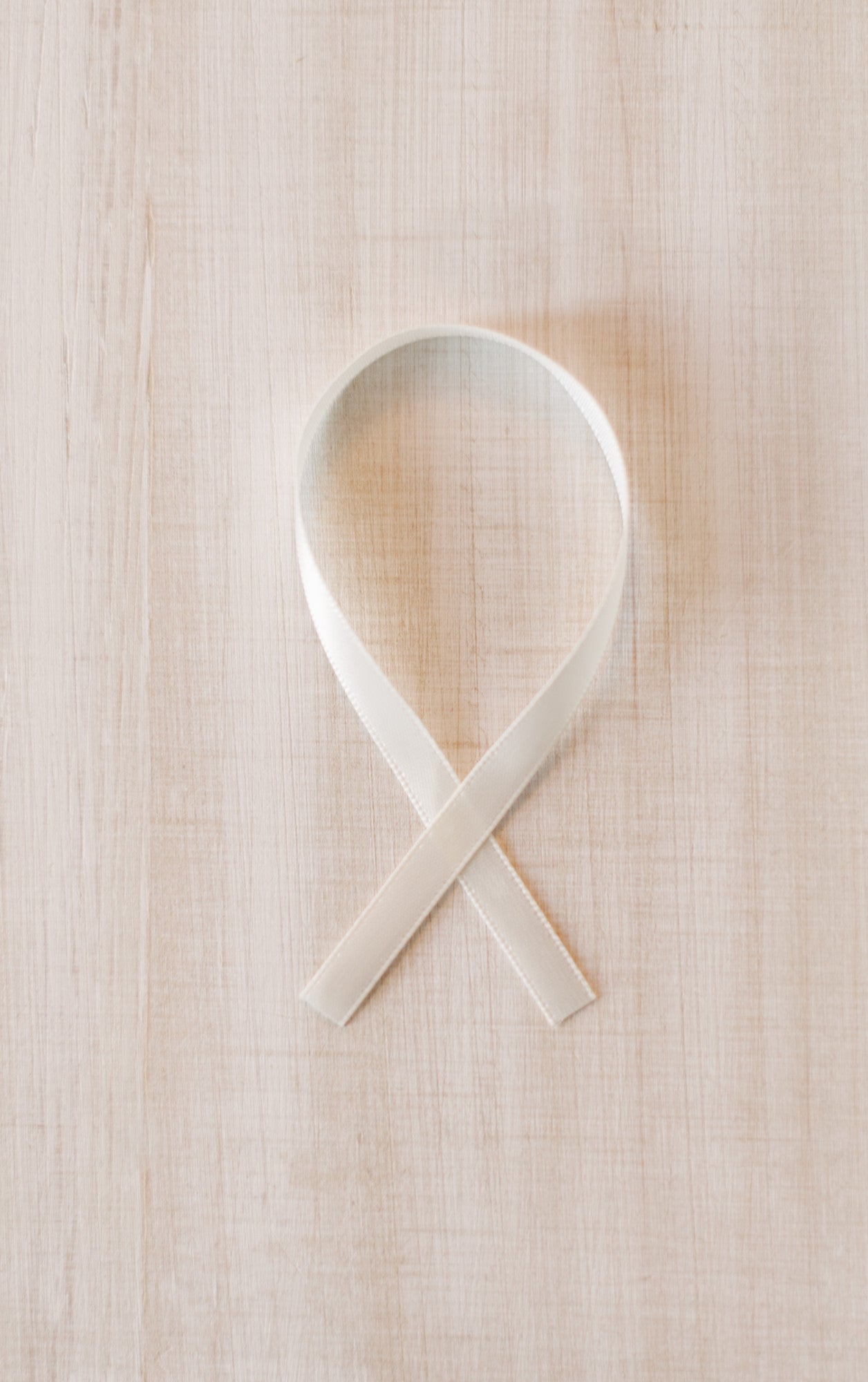 White ribbon forming an elegant loop against a light wooden surface.